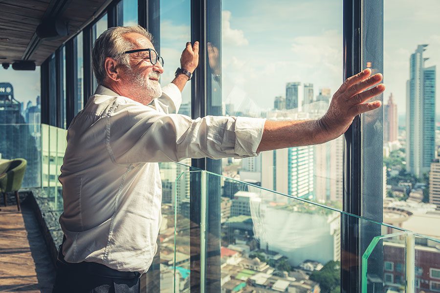 Business Insurance - View of a Mature Business Man Standing in His Office Looking Out the Glass Windows Out into the City