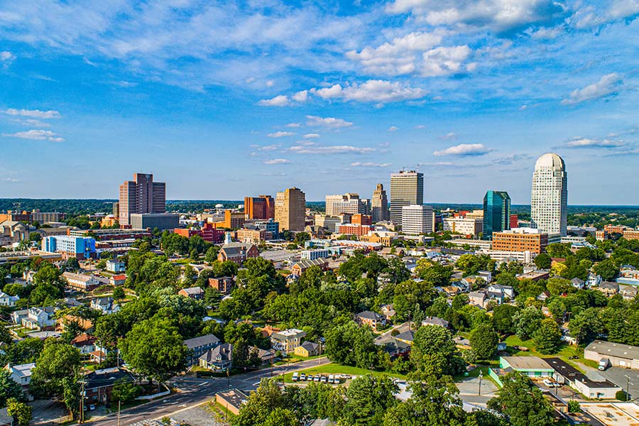 Winston-Salem NC - Aerial View of Downtown Winston-Salem Skyline Against a Blue Sky with Surrounding Homes and Commercial Buildings